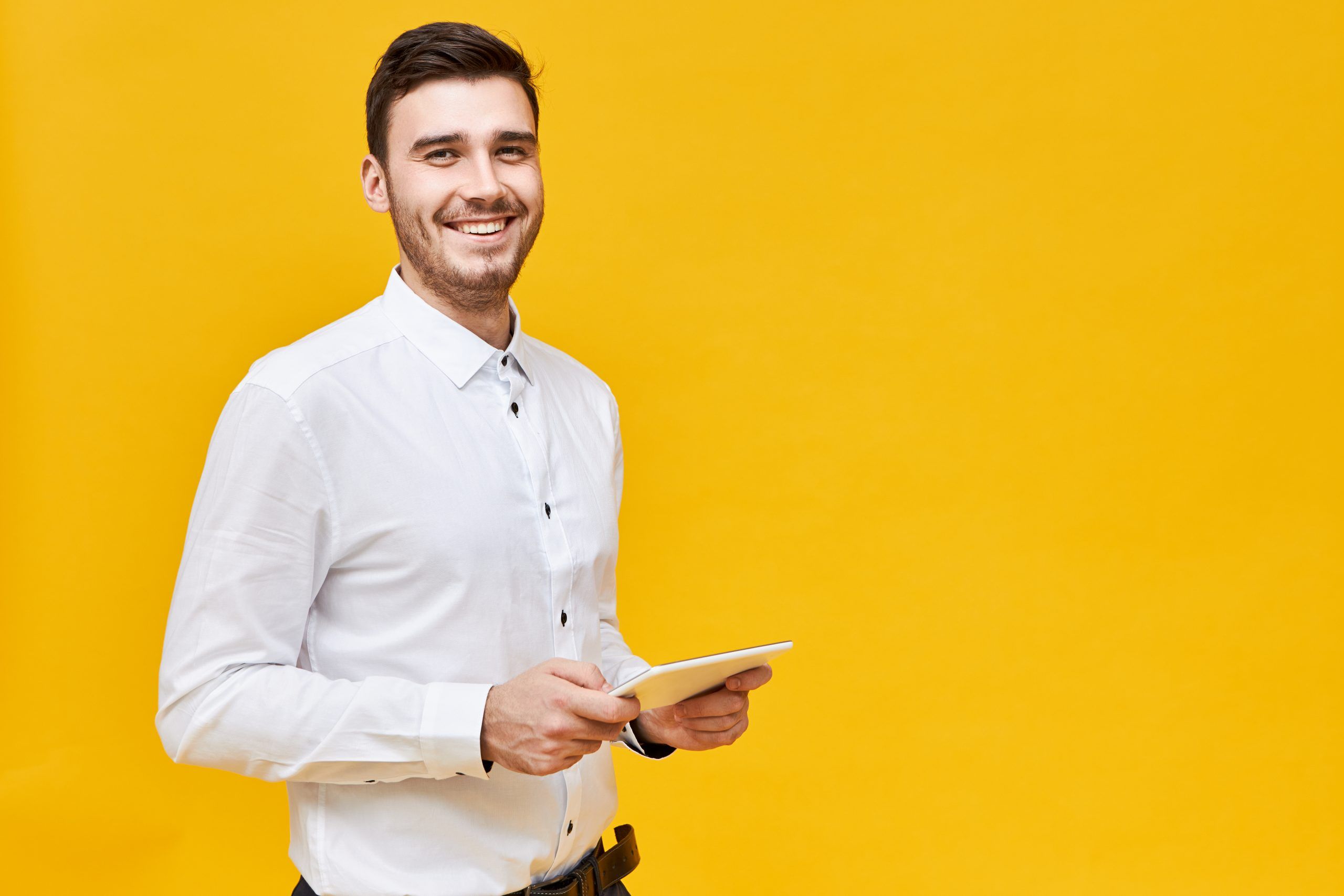 picture of handsome confident young man in white shirt holding generic digital tablet and smiling broadly enjoying playing games using online application technology entertainment and gaming scaled